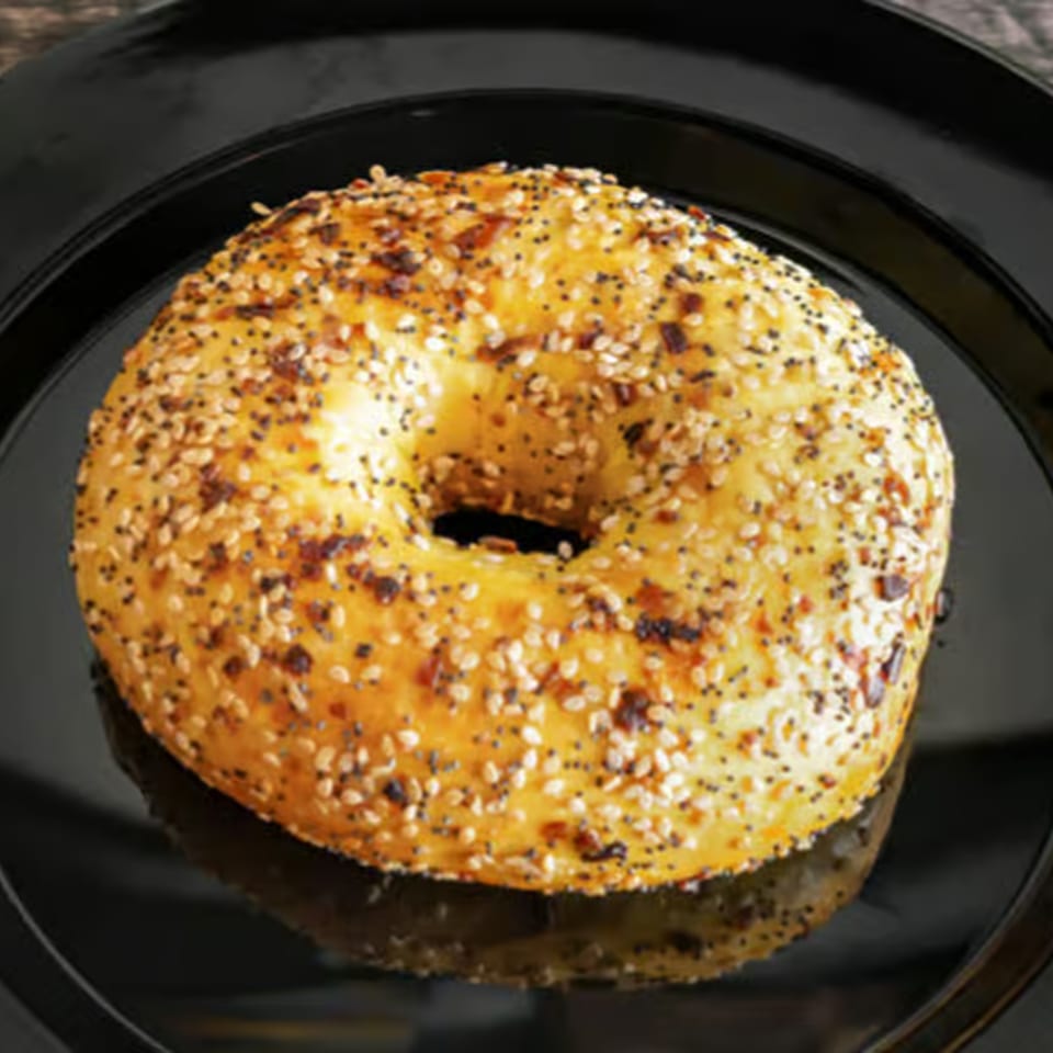 Everything bagel from Rocket Bagels Deli & Catering, covered in seeds, on a black plate.